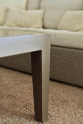 Pata de una mesa de exterior en aluminio con un sofá de fibras al fondo.