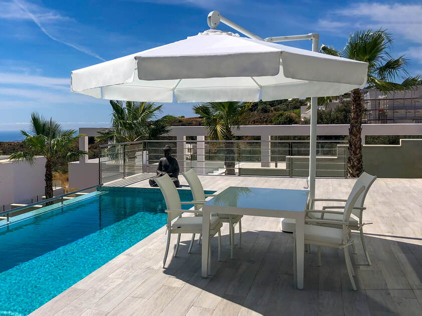 parasol reclinable en zona de piscina con mesa de aluminio y cristal y sillones canvas de exterior